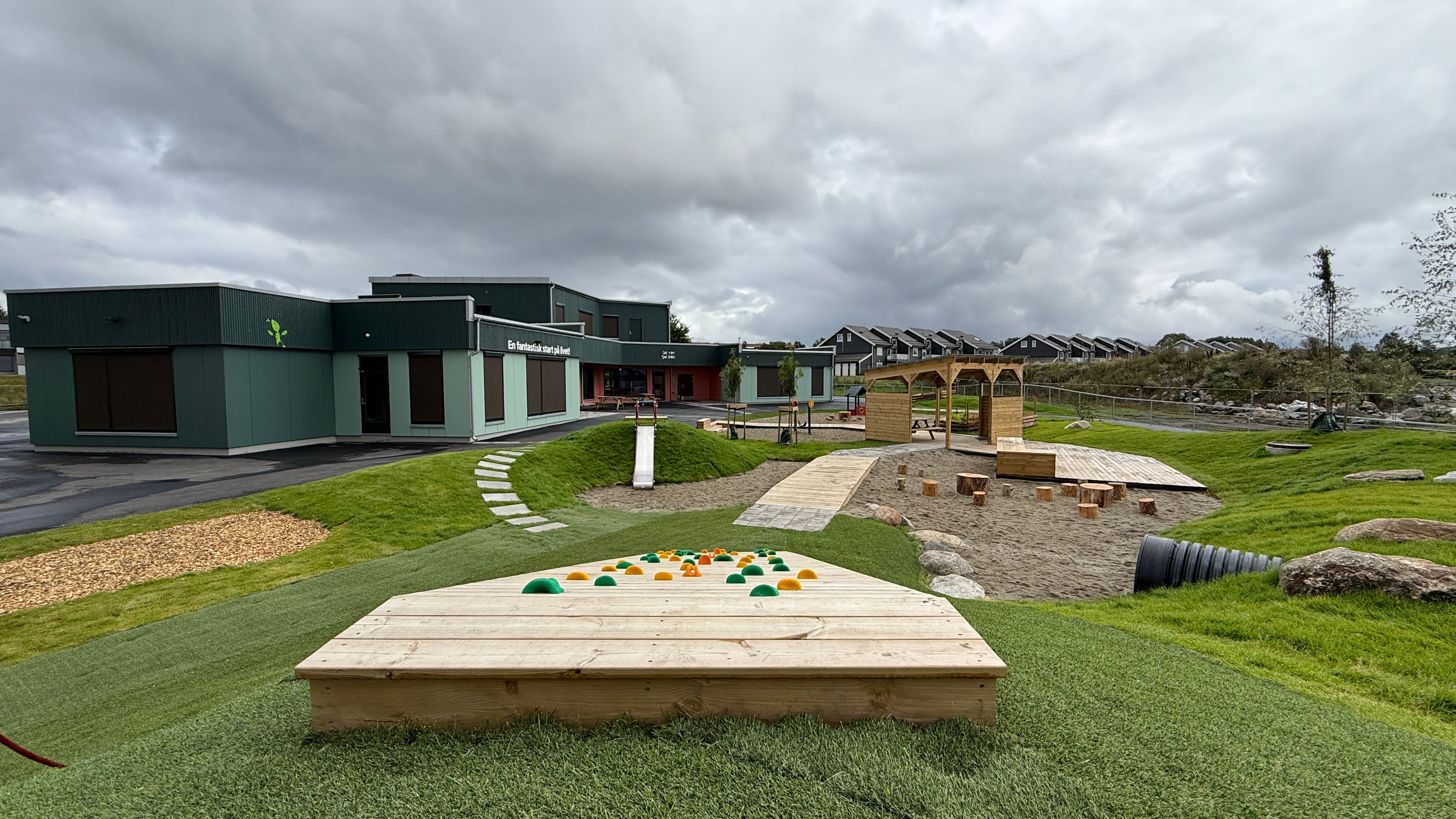 a wooden sandbox is sitting on top of a lush green field in front of a building .
