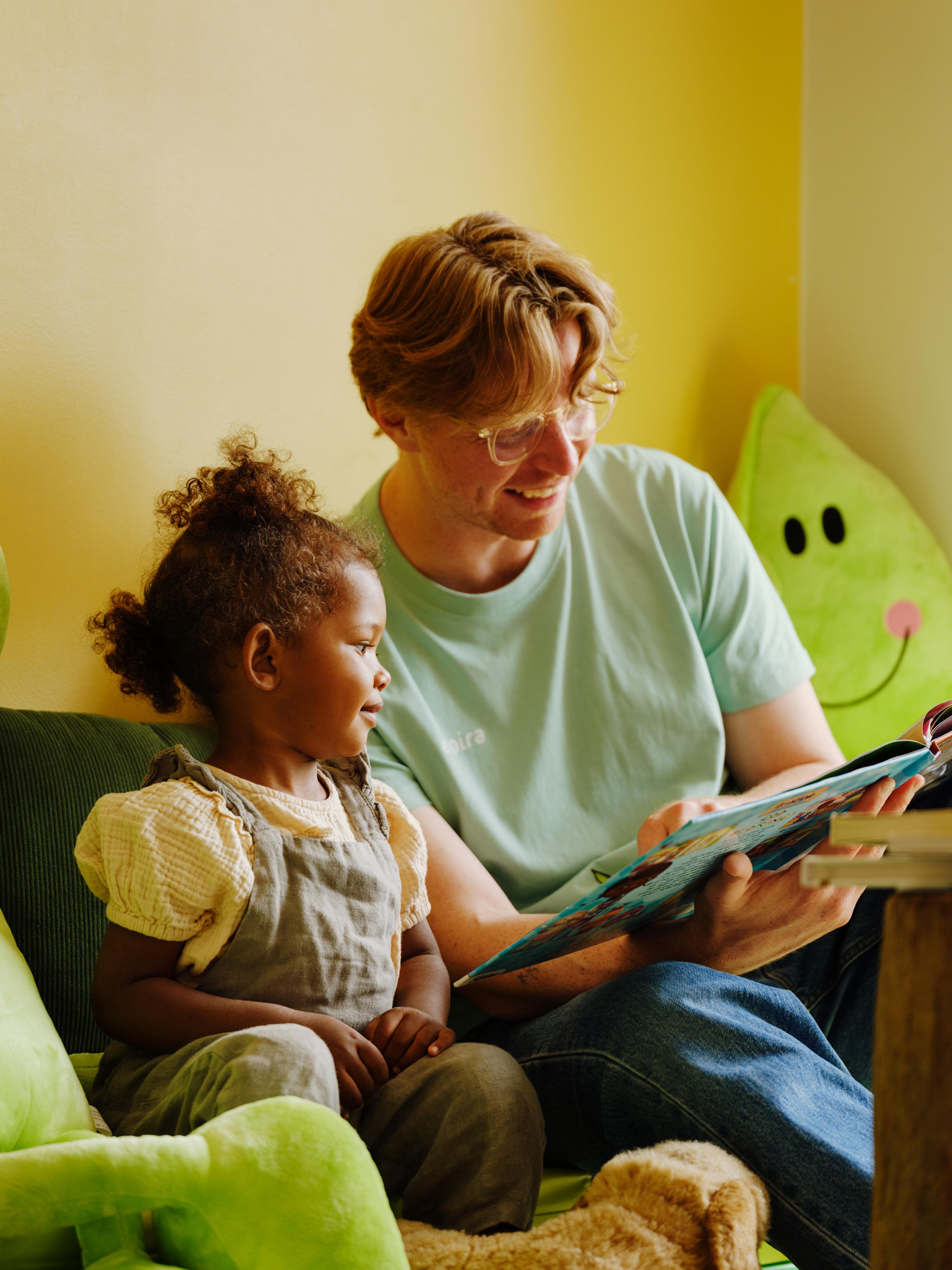 En mann som leser en bok for en liten jente i barnehagen