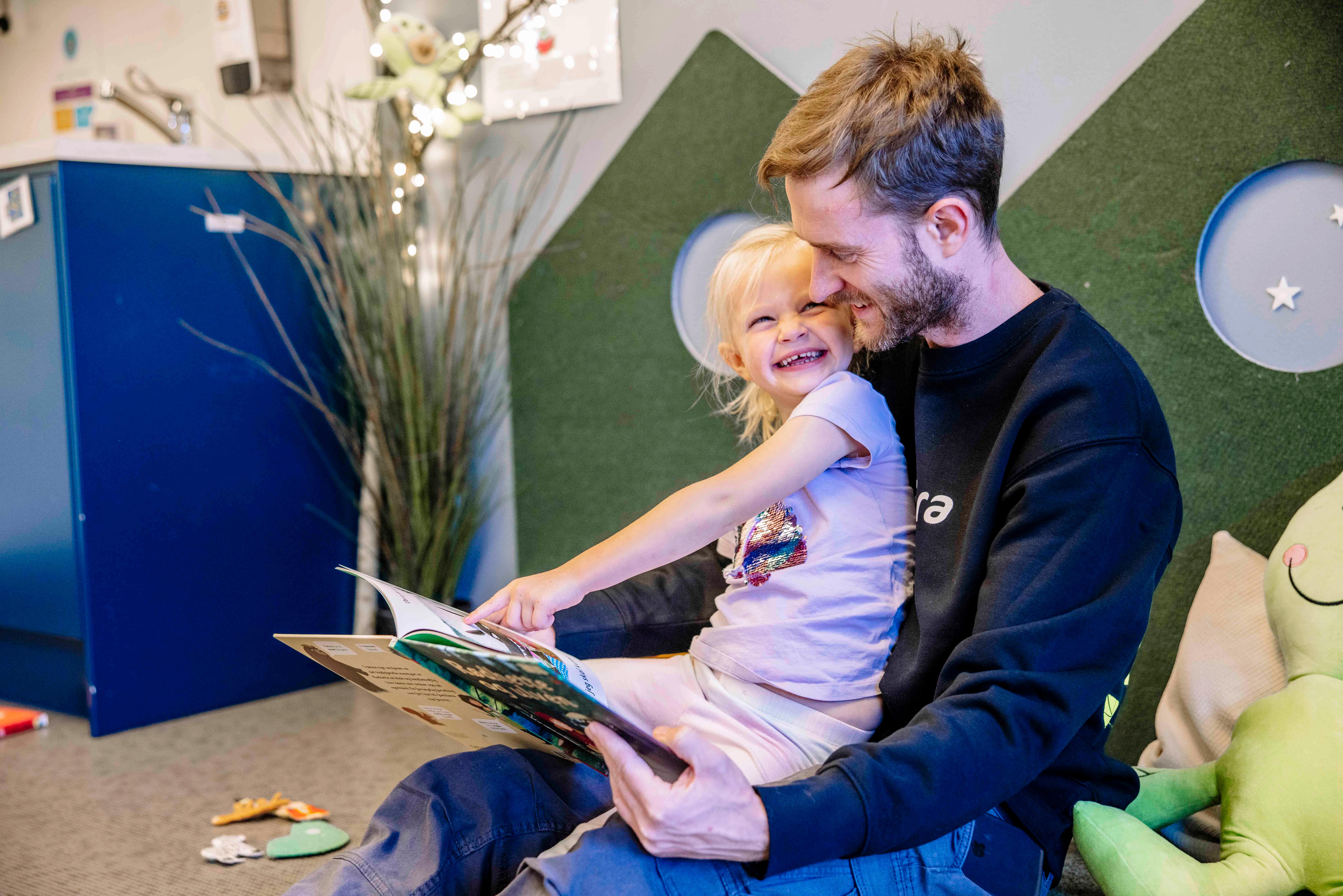 En mann som leser en bok for en liten jente i barnehagen
