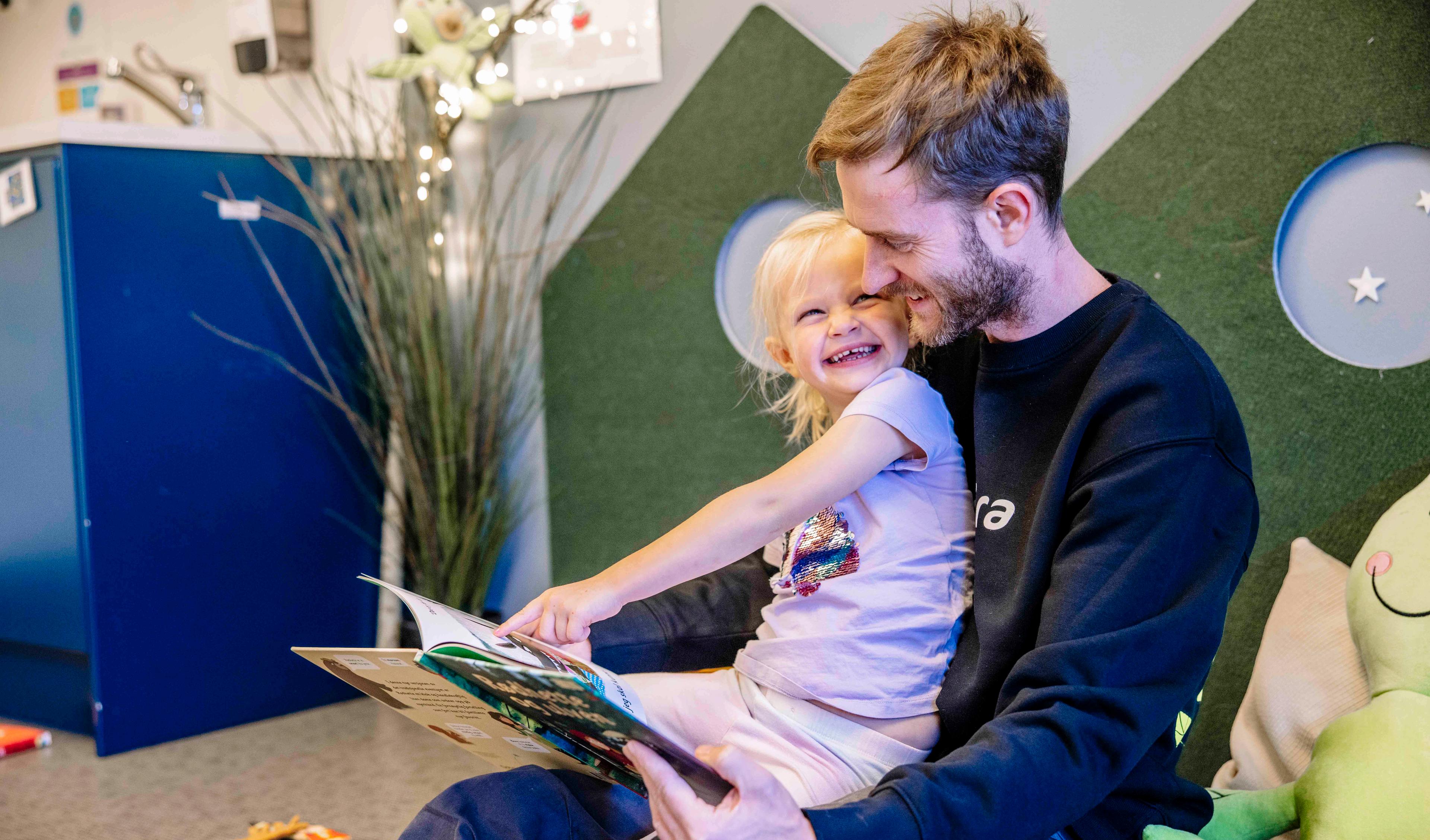 En mann som leser en bok for en liten jente i barnehagen