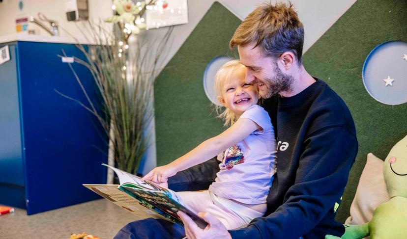 En mann som leser en bok for en liten jente i barnehagen