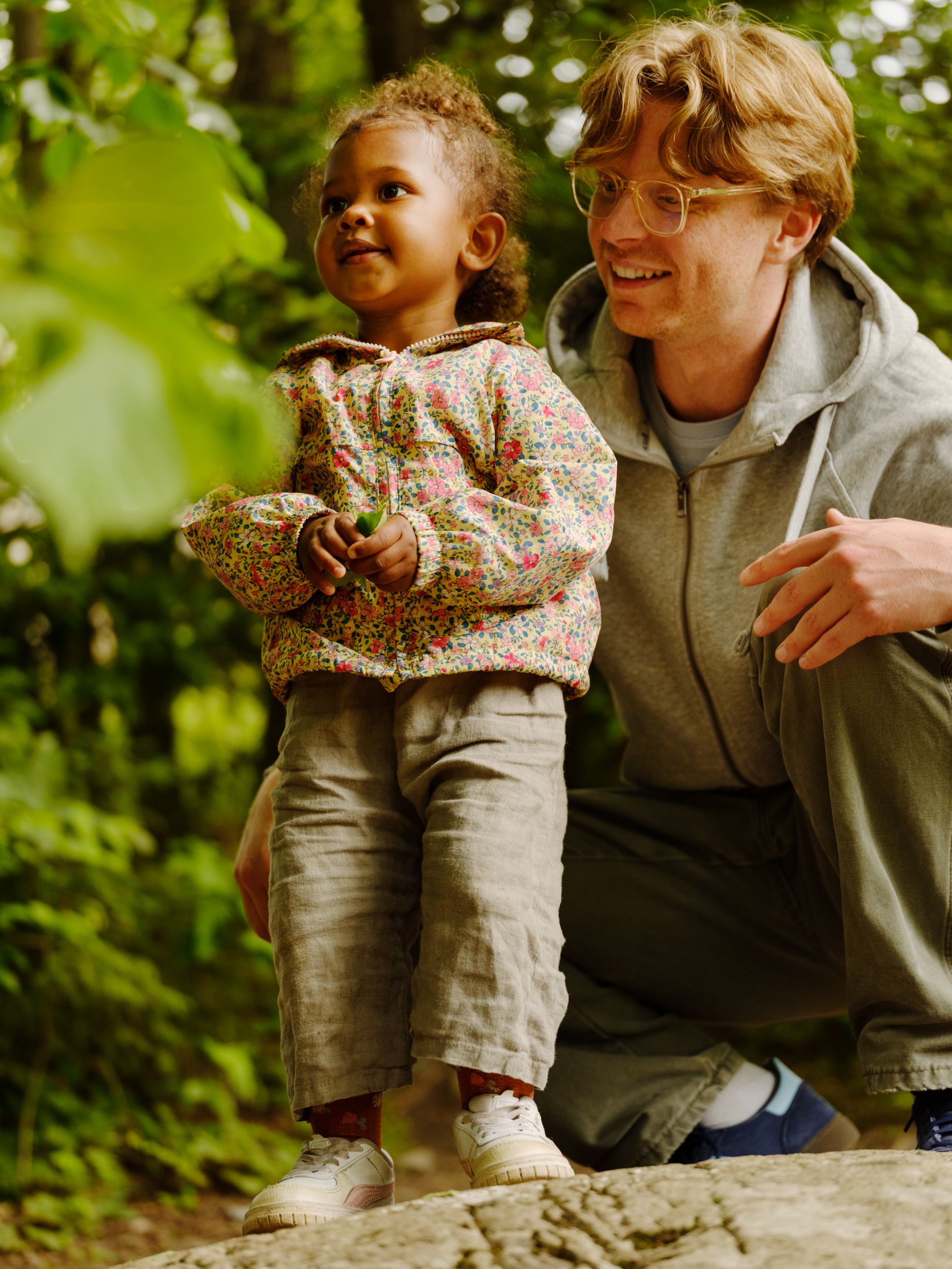 a man and a little girl are kneeling on a rock in the woods .