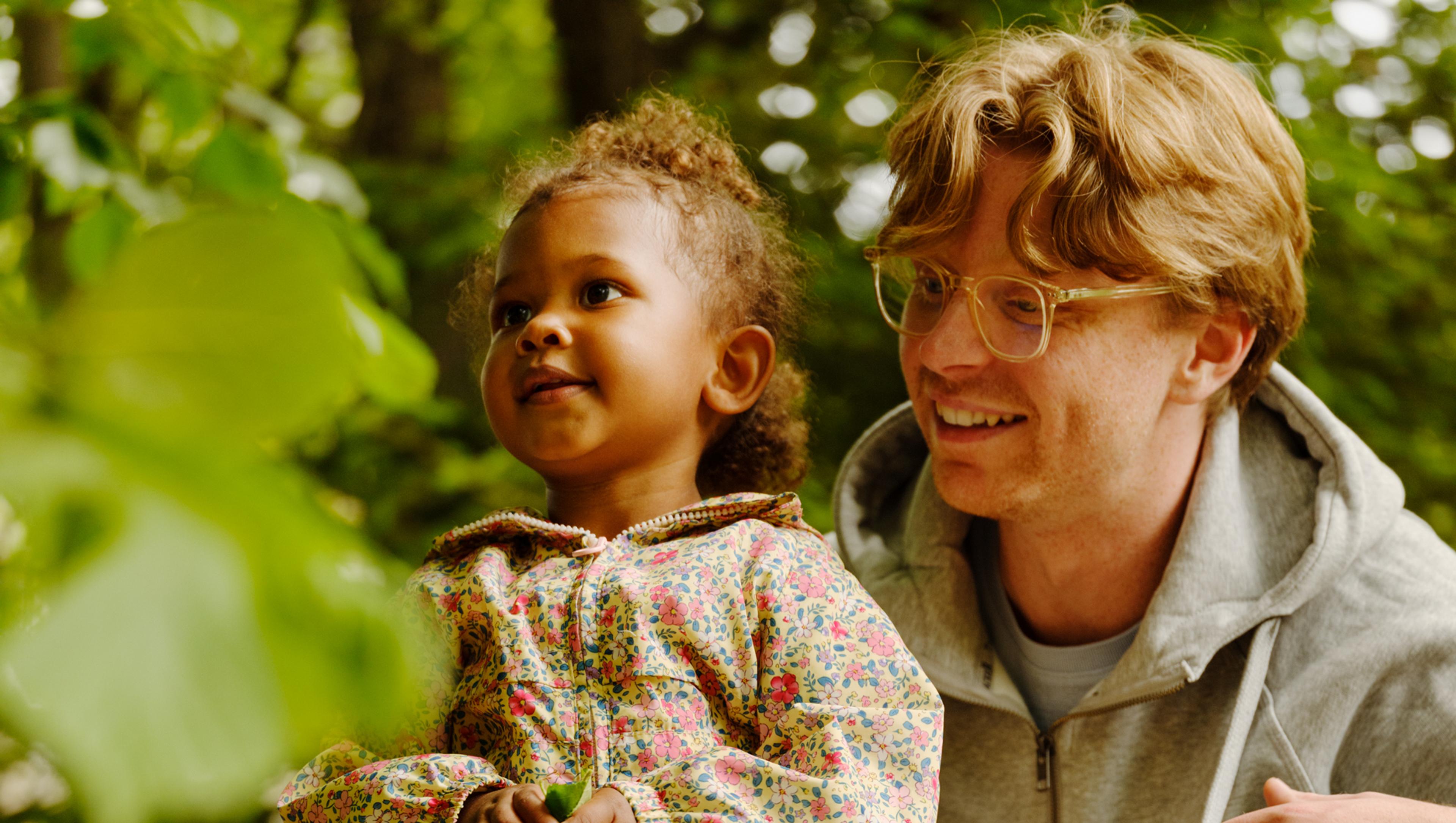 a man and a little girl are kneeling on a rock in the woods .