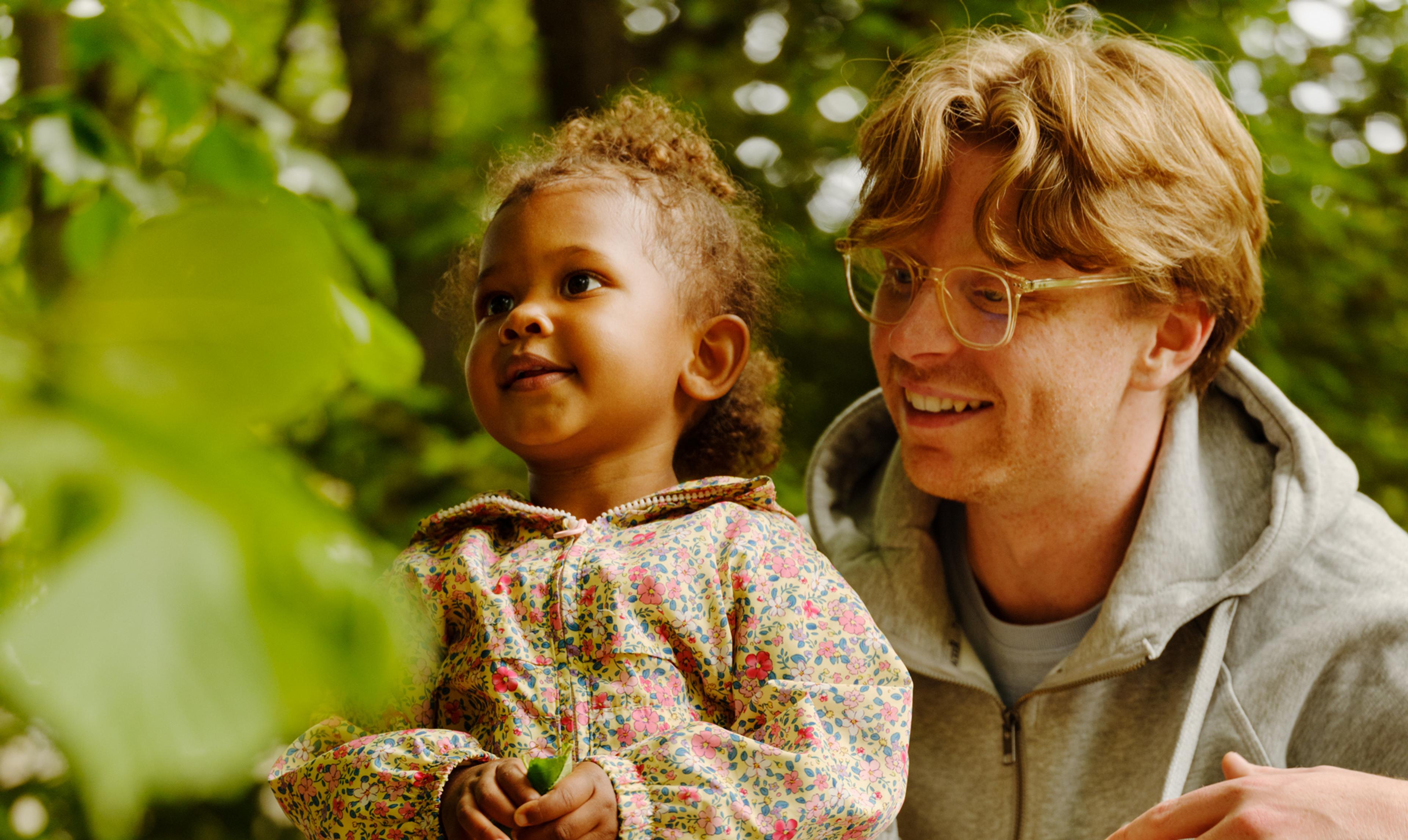 a man and a little girl are kneeling on a rock in the woods .