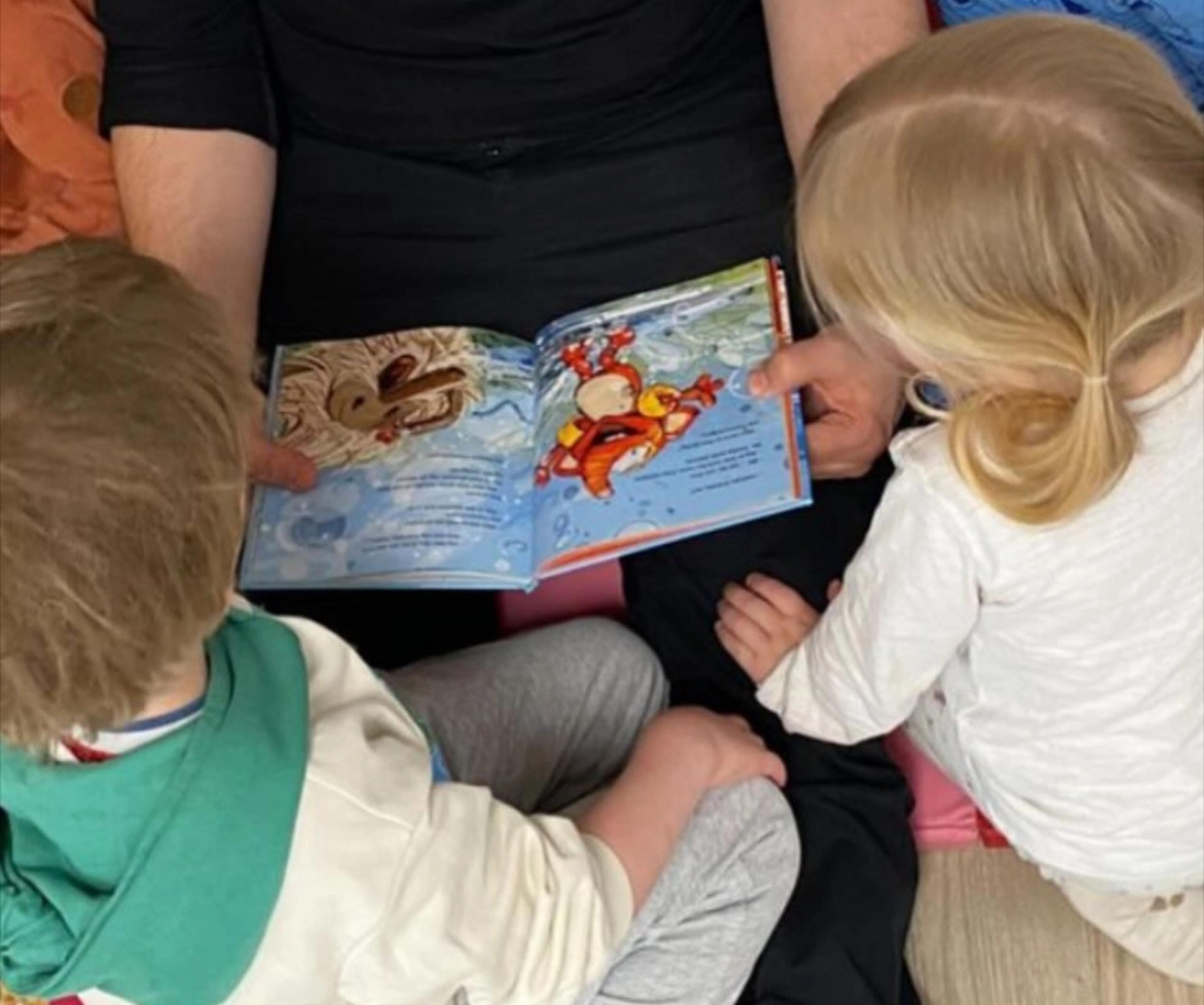 Barn som leser bok sammen med ansatt i Espira Kystad gård