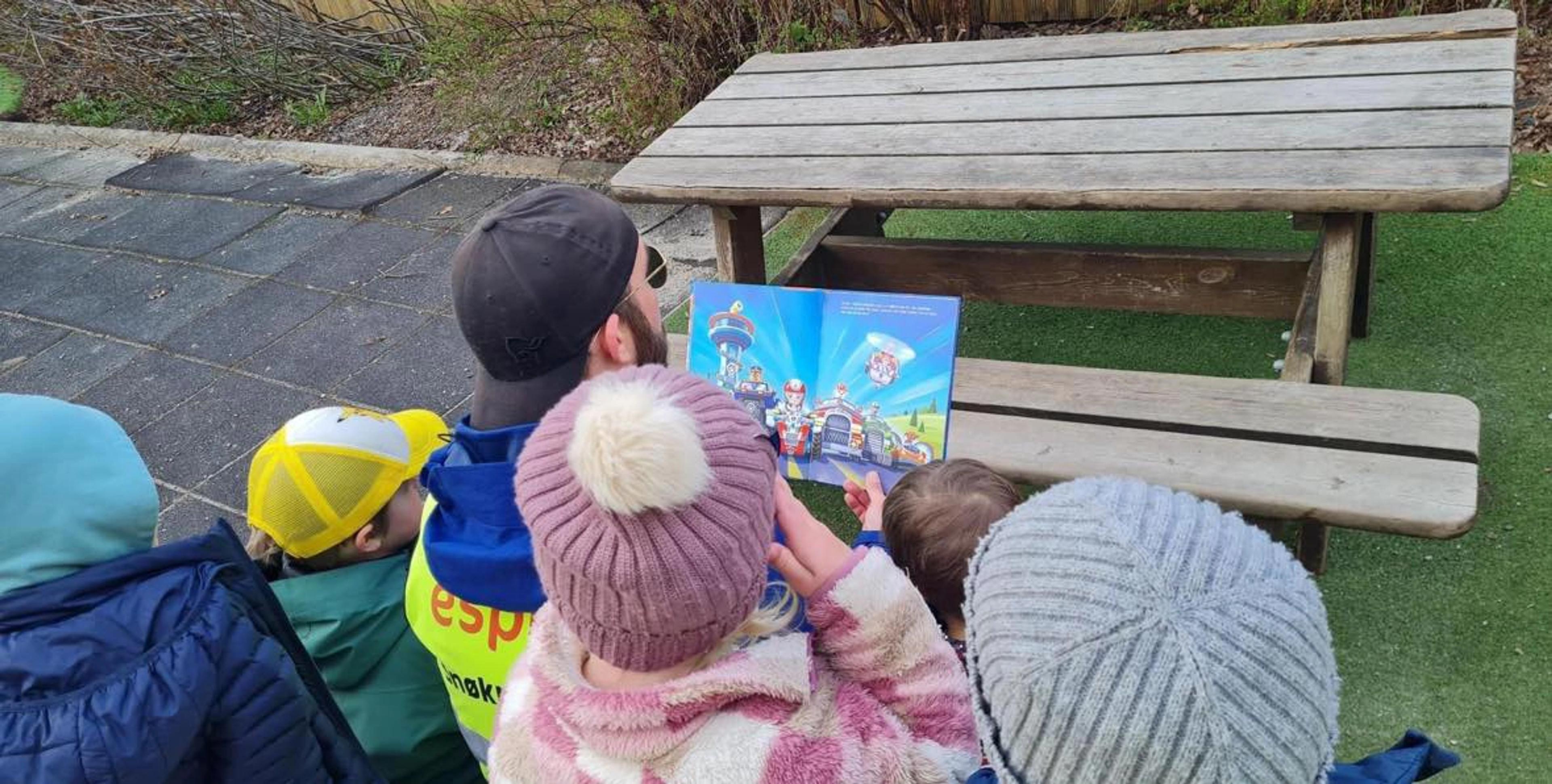 Ansatt som leser bok for barn ute i Espira Kuventræ