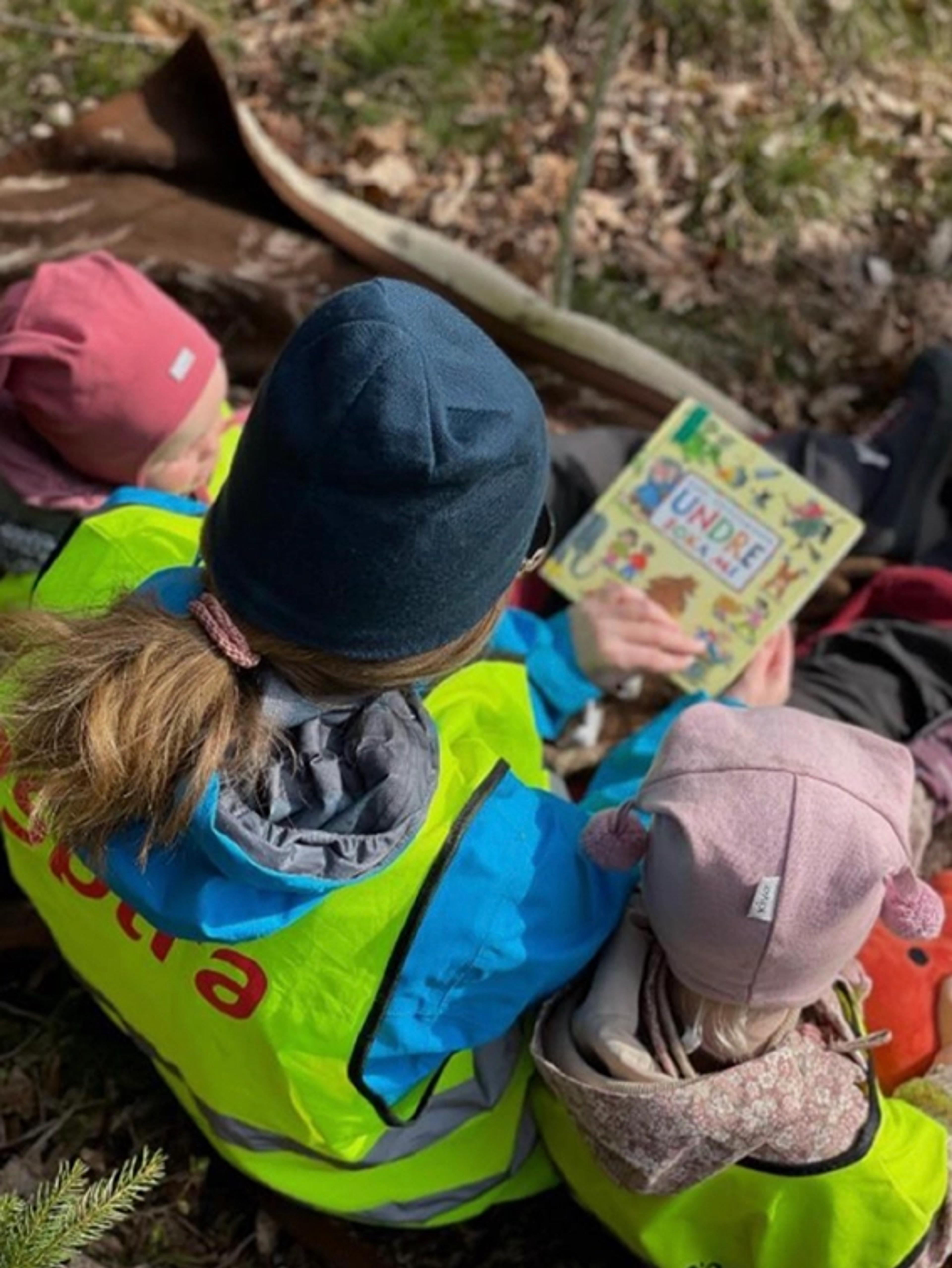 Barn og ansatte som leser bok ute i skogen i Espira Lindesnes