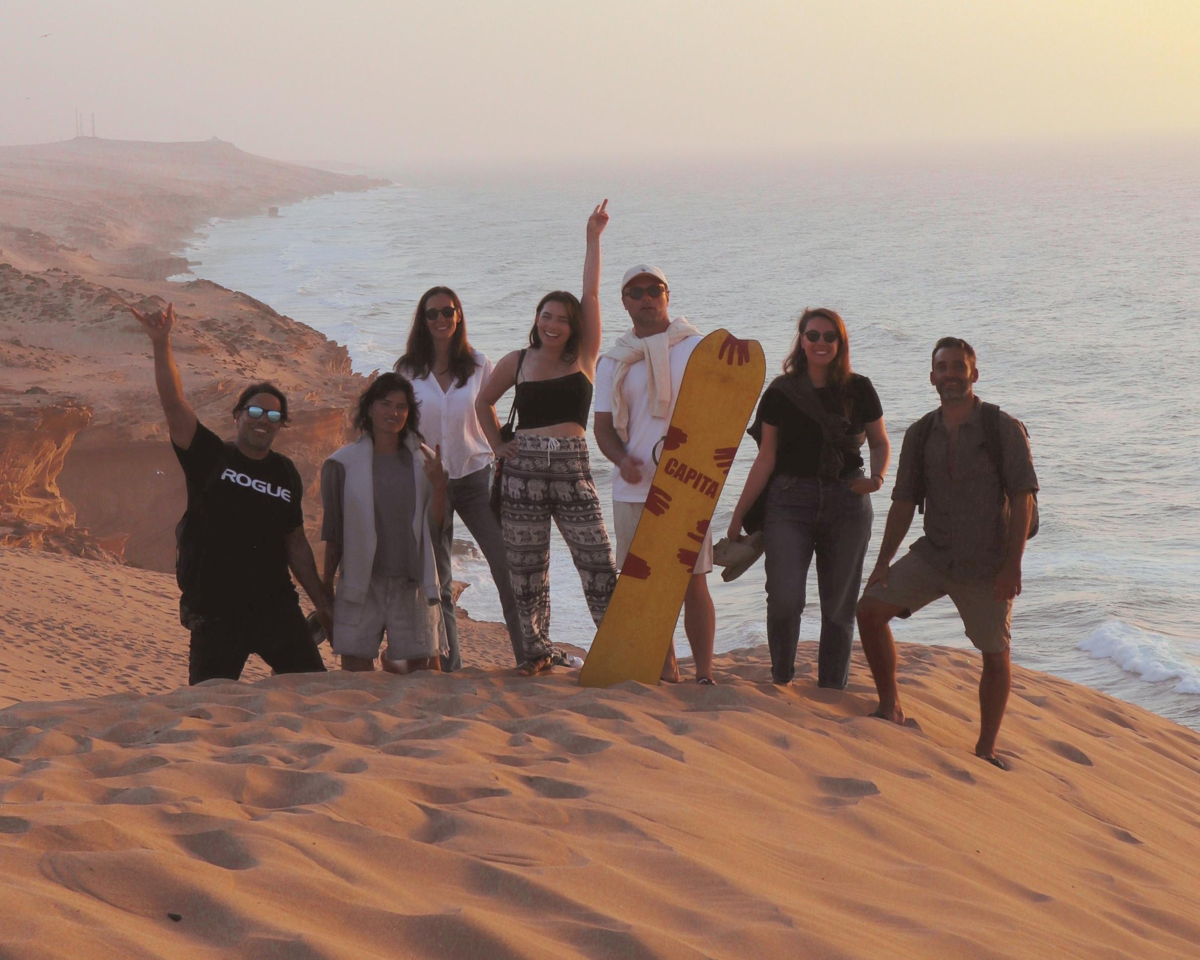 Group of friends celebrating on the desert dunes at sunset during a Sea Me Smile surf trip