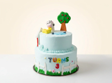 Two-tier pale blue farmyard cake with fondant cow, apple tree, duck pond, white picket fence and colourful lettering