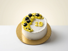 White cake with a crescent of lemon-yellow buttercream rosettes, fresh blueberries and a piped number nineteen