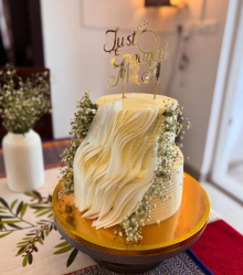 Elegant two-tier white engagement cake with ruffled chocolate shards, baby's breath flowers, and gold Just Engaged topper
