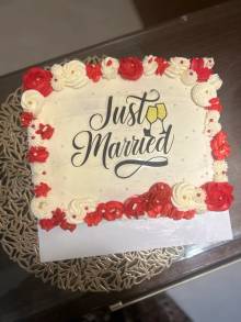 Rectangular cream cake bordered with red and white piped roses and a black Just Married topper