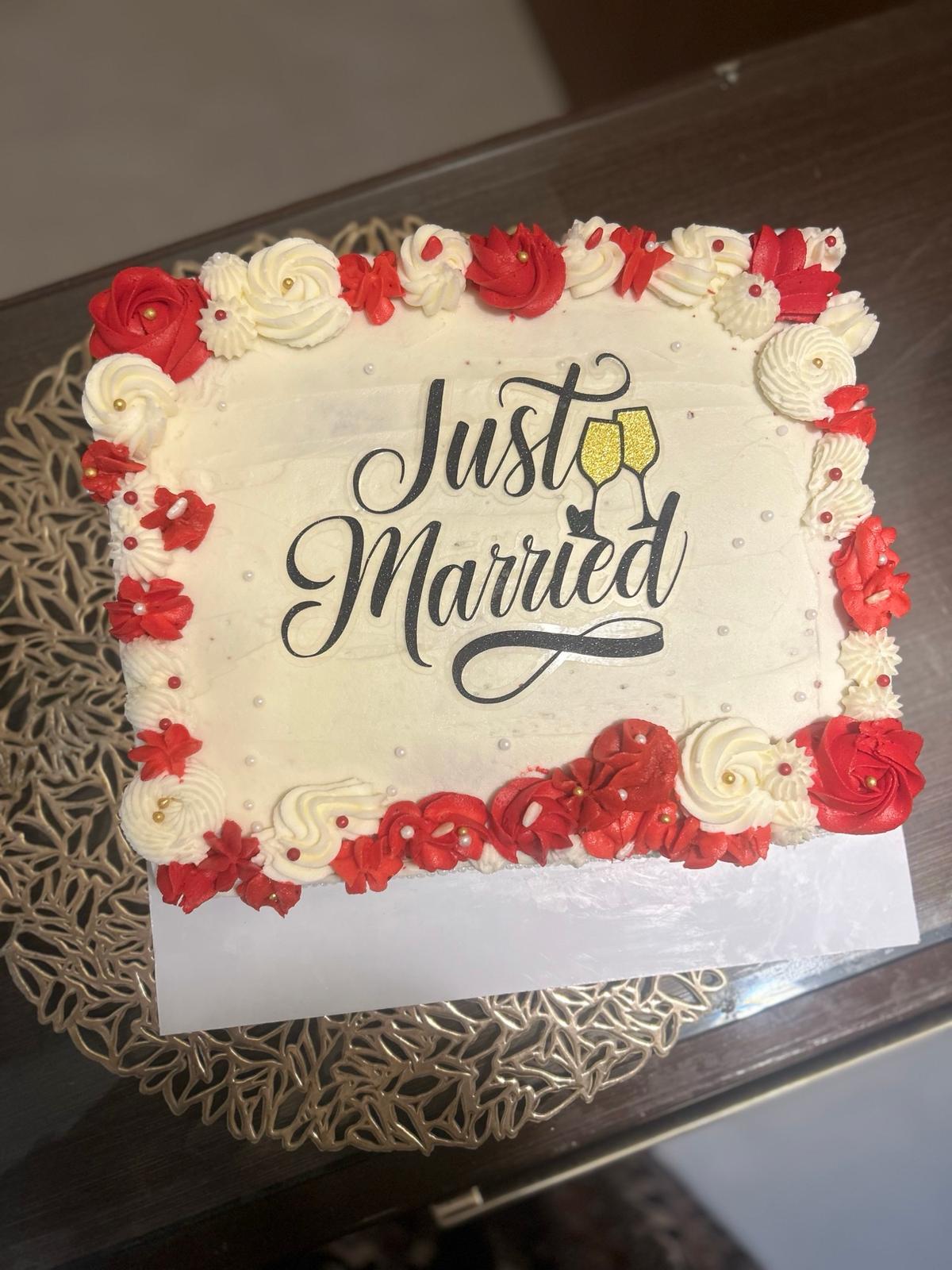 Rectangular cream cake bordered with red and white piped roses and a black Just Married topper