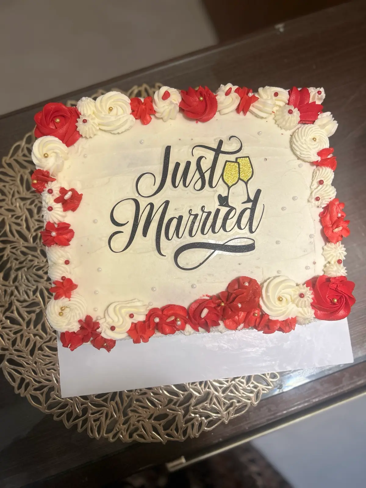 Rectangular cream cake bordered with red and white piped roses and a black Just Married topper