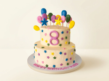 Two-tier cream cake covered in colourful fondant stars with balloon and star toppers and a number topper