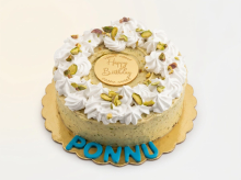 Round buttercream cake with a whipped-cream garnish and crushed pistachios around a gold Happy Birthday disc