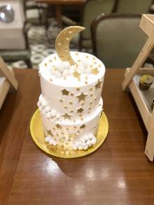 Two-tier white cake decorated with gold stars, white cloud puffs and a crescent moon topper