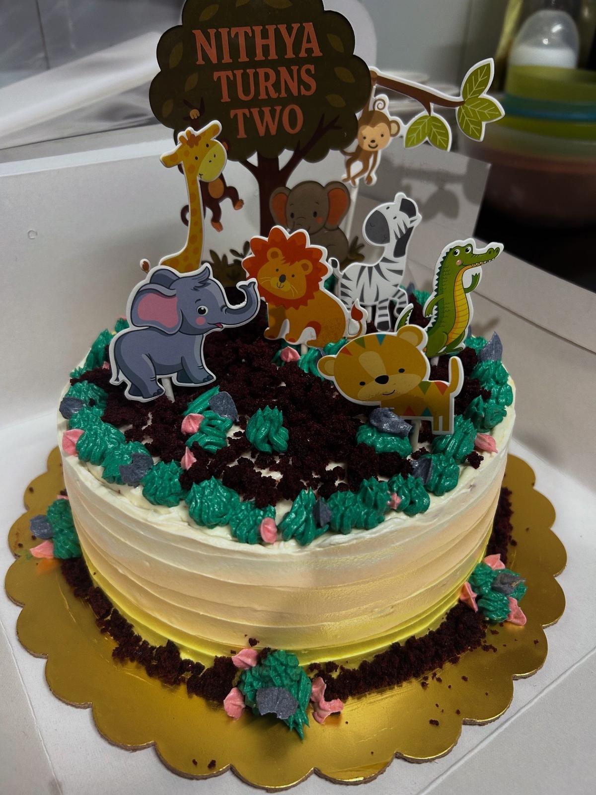 Cream buttercream cake with chocolate-crumb soil, piped green grass and cartoon jungle animal toppers around a tree topper