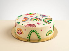 White buttercream cake hand-piped with rainbow arches and dots in natural plant-based colours