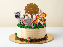 Cream buttercream cake with chocolate-crumb soil, piped green grass and cartoon jungle animal toppers around a tree topper