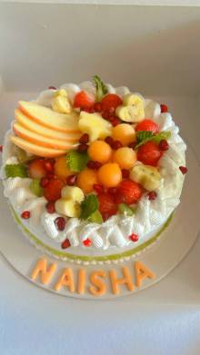 White cream cake topped with fresh apple slices, melon balls, banana and pomegranate with a personalised name