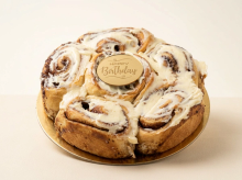 Round pull-apart cinnamon roll cake with cinnamon swirls topped with cream cheese frosting on a gold cake board