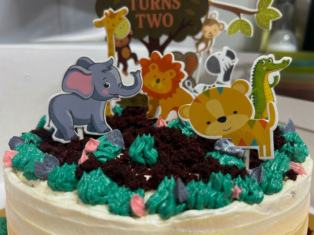 Cream buttercream cake with chocolate-crumb soil, piped green grass and cartoon jungle animal toppers around a tree topper