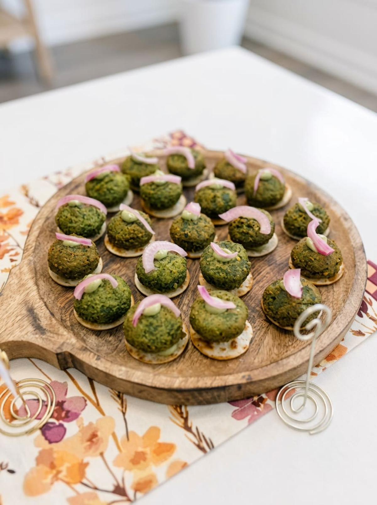 Green herb kebab bites on crackers with pickled onion on a wooden board