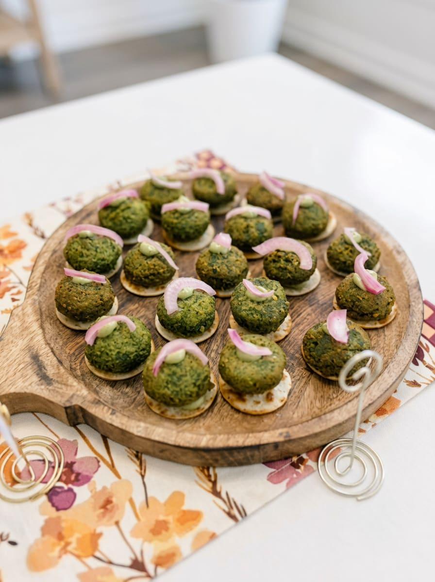 Green herb kebab bites on crackers with pickled onion on a wooden board