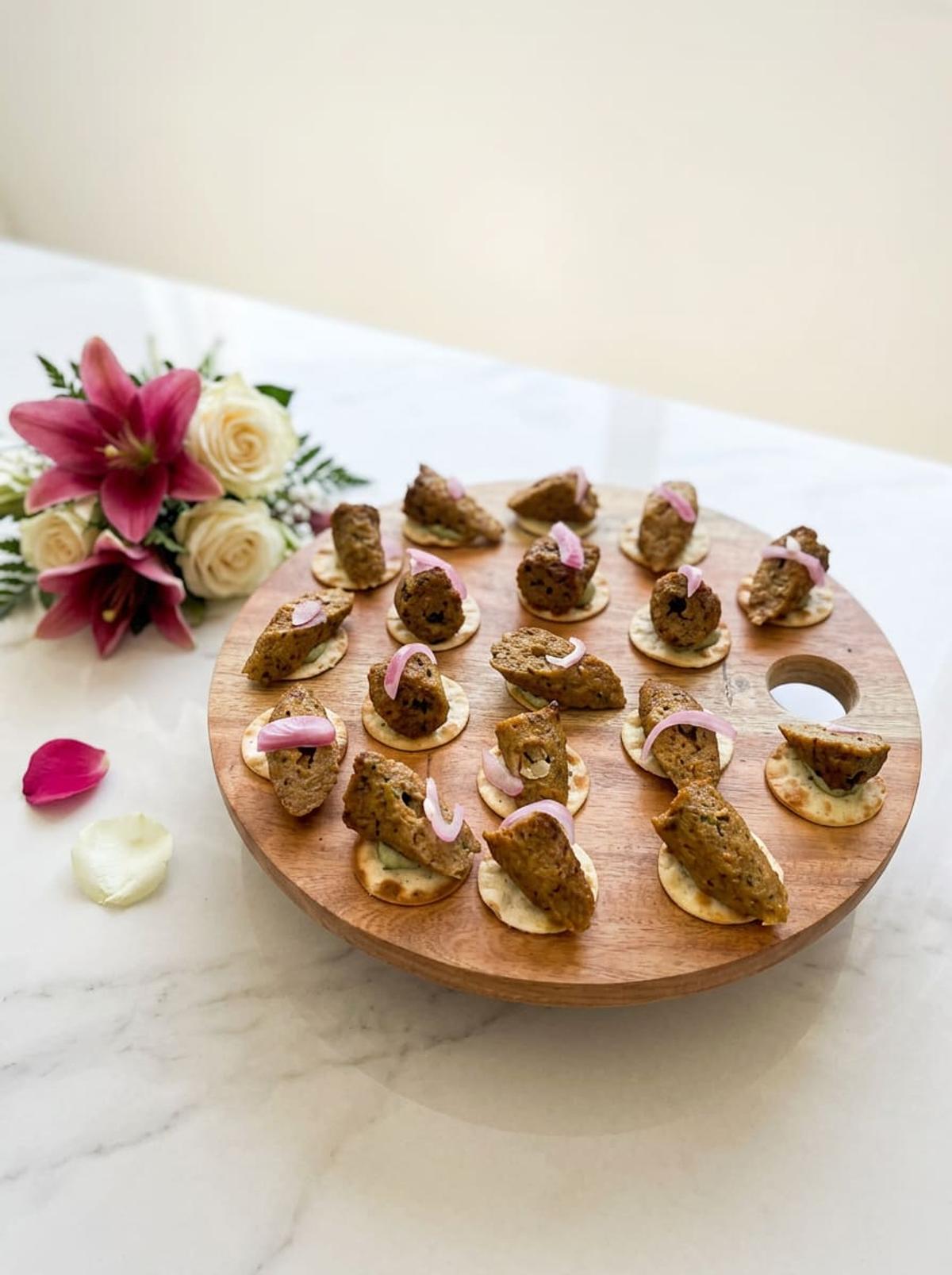 Round wooden board of canapés with pickled onion, styled with a lily posy