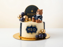 Buttercream birthday cake with a fondant teddy bear, gold and navy spheres and an HBD plaque