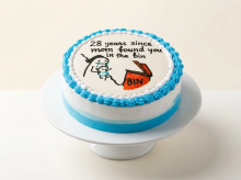 White cake with a blue piped border and a hand-painted cartoon doodle and message on top