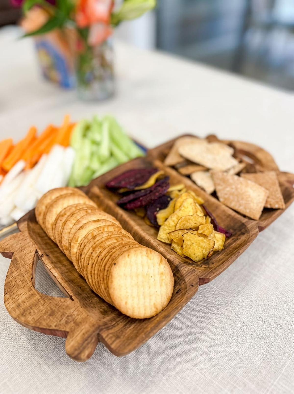 Wooden tray of crackers and vegetable chips with rainbow crudités
