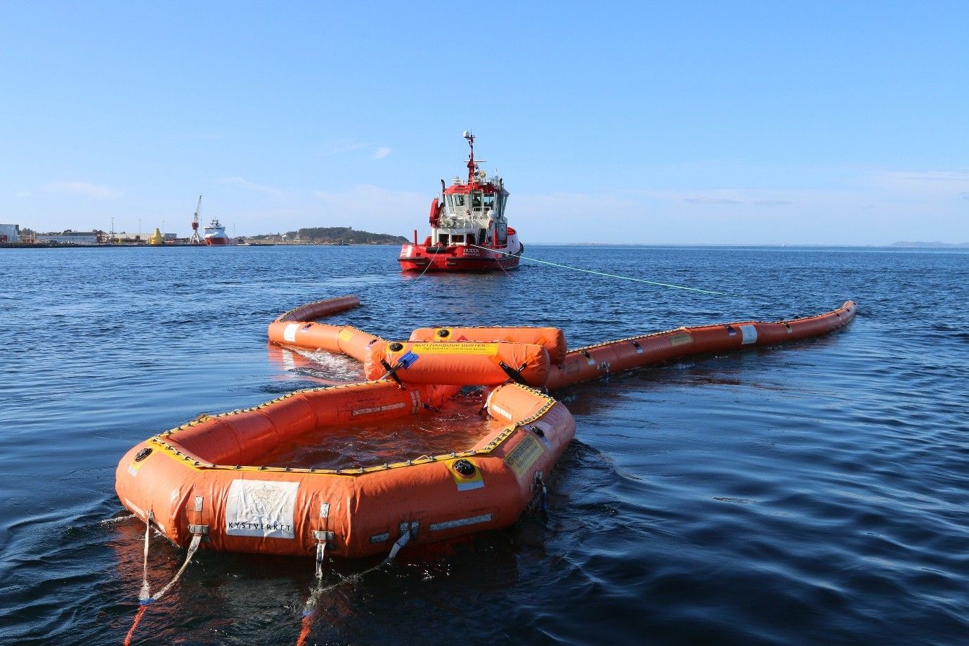 Oransje oljelenser settes ut av et skip på havet. Flere skip i bakgrunnen.
