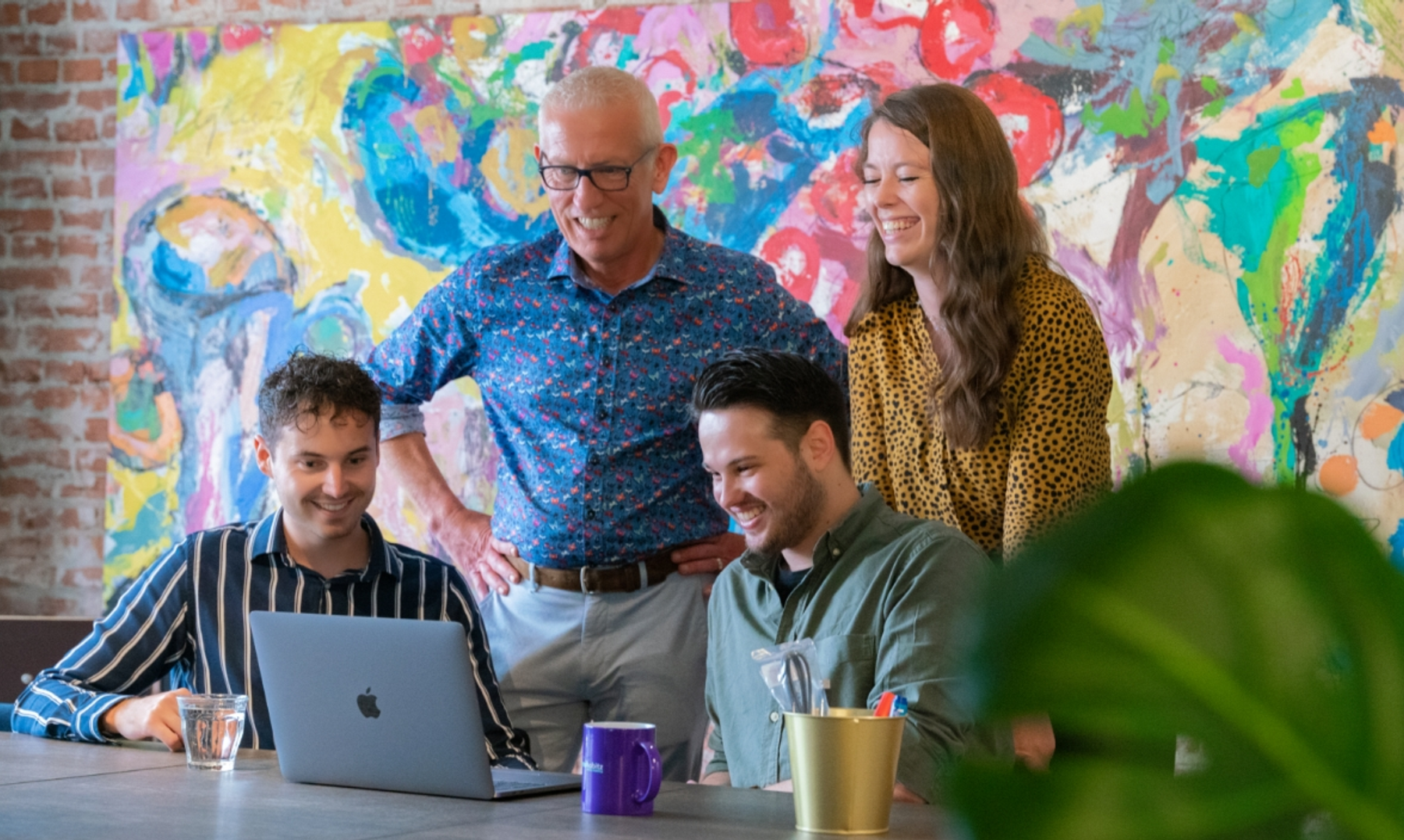 4 persons looking cheerfully together on a laptop