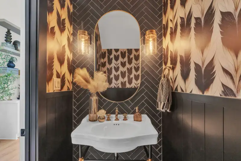 Powder room with feather-print wallpaper, herringbone tile, and a white console sink on black metal legs.