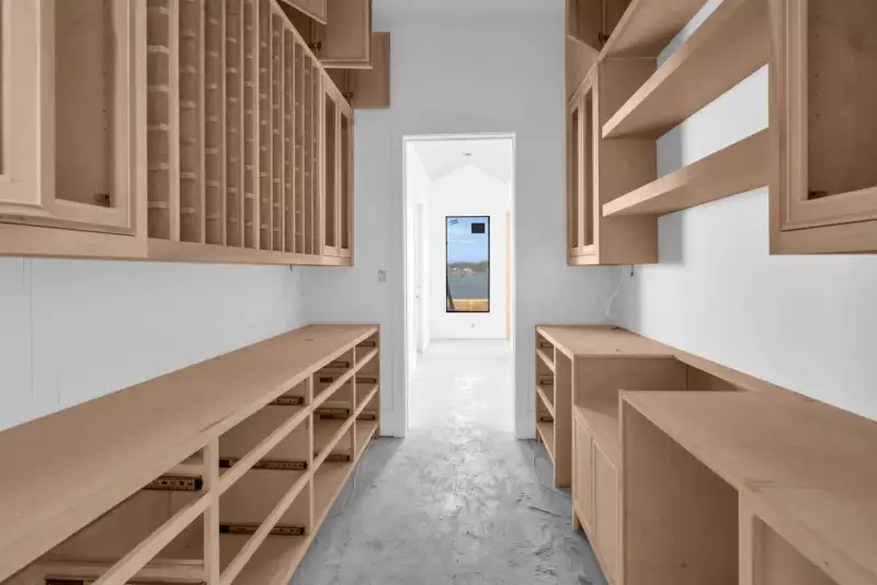 Narrow pantry lined with wood cabinets and wine storage, with a hallway and window at the far end.