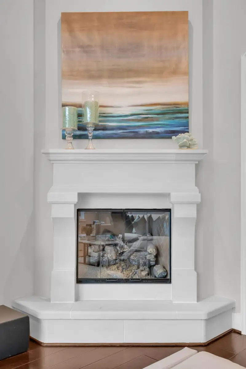 Fireplace with a white painted surround, a glass-fronted firebox, and an abstract landscape painting.