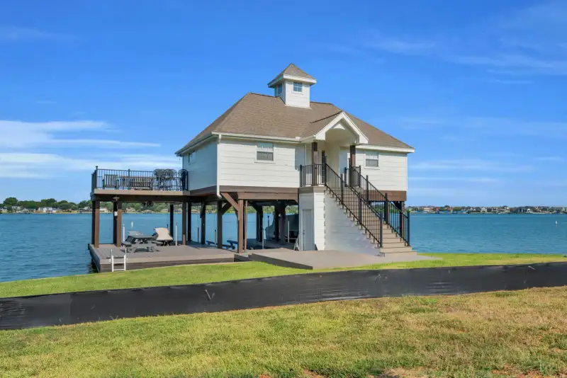 Boathouse on pilings with white siding, a deck below, and an exterior staircase.