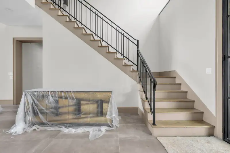 Staircase with a black metal railing, wood treads, and covered furniture at the base.