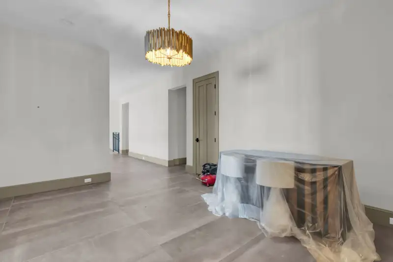 Room with a gold chandelier, covered furniture, and a doorway into an adjoining space.