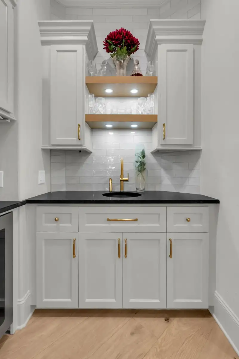 Bar area with a gold faucet over a sink, a dark countertop, and open wood shelves above.
