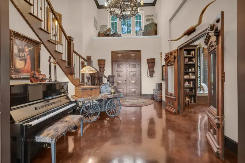 Two-story entry hall with a wood staircase, a black upright piano, a longhorn skull, and polished reddish-brown floors.