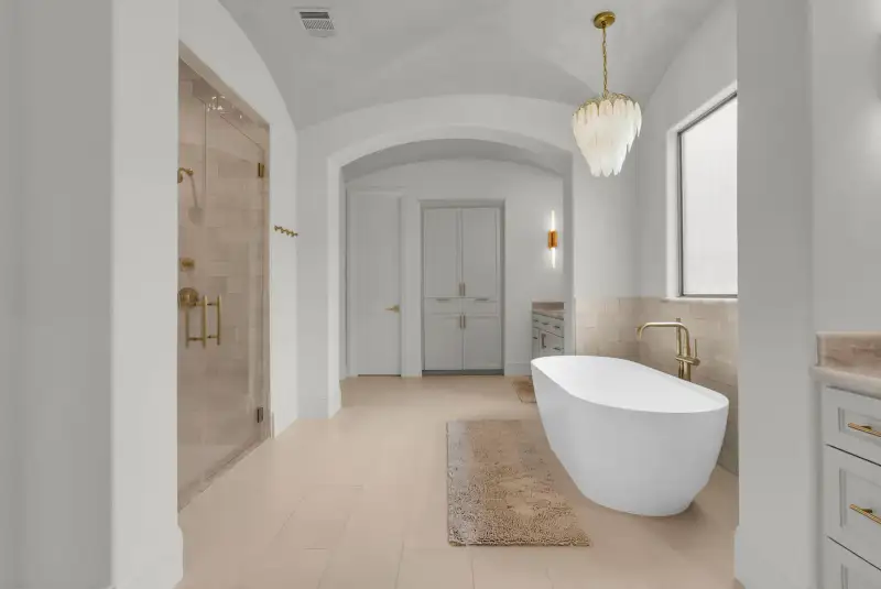 Primary bath with a freestanding tub, a glass-enclosed shower, and a tall cabinet in an arched niche.