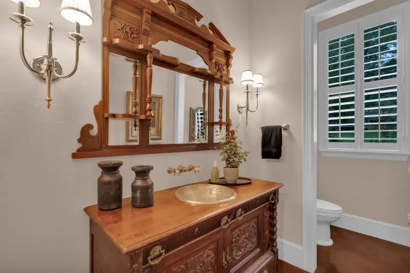 Powder room with a brass basin on a carved wood vanity, wall sconces, and an ornate framed mirror.
