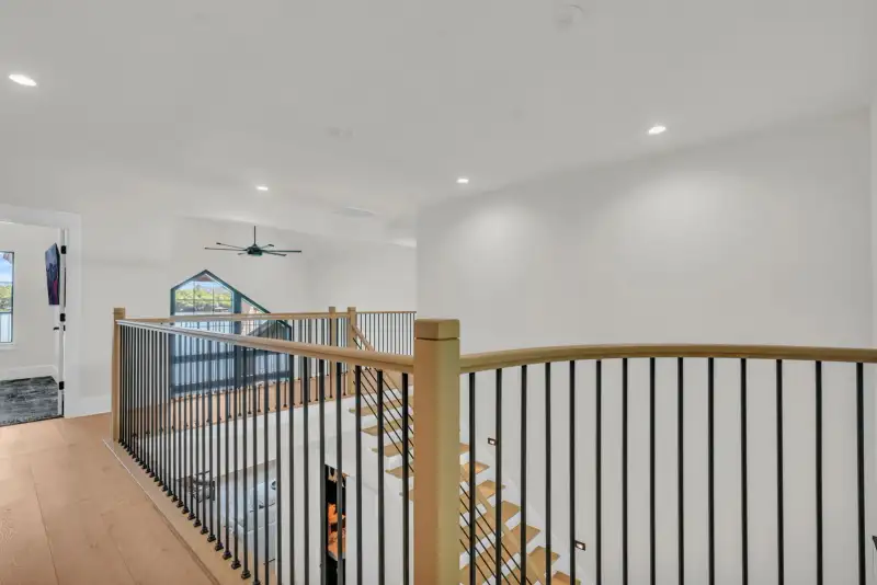 Upper landing with a wood handrail and black metal balusters, with recessed ceiling lights.