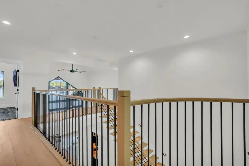 Upper landing with a wood handrail and black metal balusters, with recessed ceiling lights.