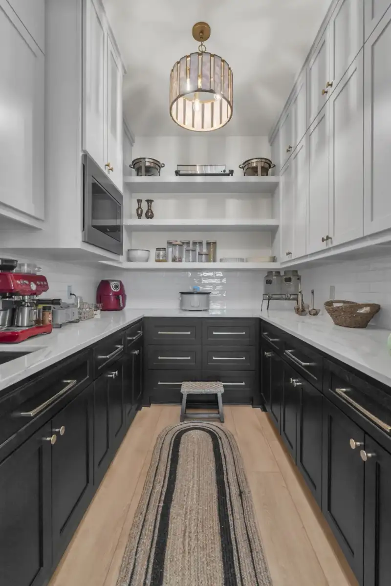 Pantry with dark lower cabinets, white upper cabinets, open shelving, and a woven runner rug.