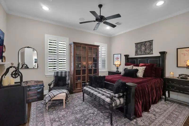 Bedroom with a black four-poster bed, red velvet bedding, a ceiling fan, plantation shutters, and a plaid bench.