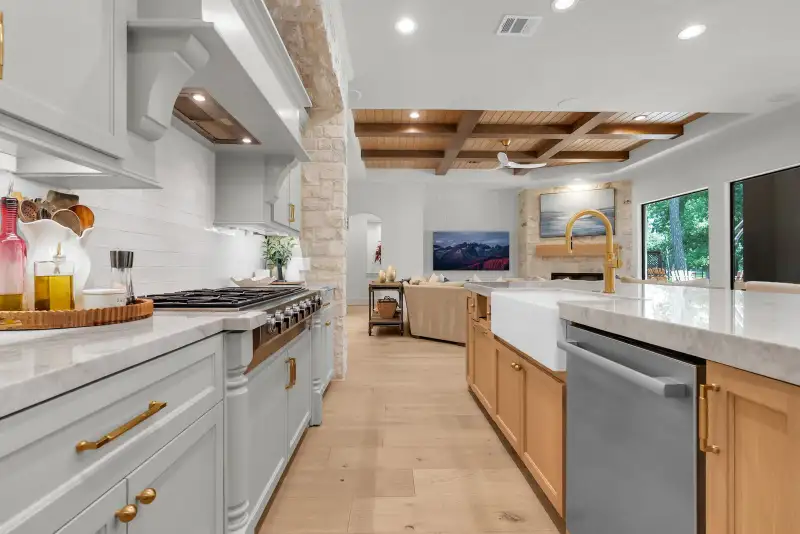 Kitchen range under a white hood beside a stone column, with a farmhouse sink island in front.